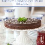 Photo collage of a Swedish Sticky Chocolate Cake (Kladdkaka) on a white lace cake pedestal on a granite countertop with a small pitcher of Raspberry Coulis on the right and fresh mint garnish in the foreground.