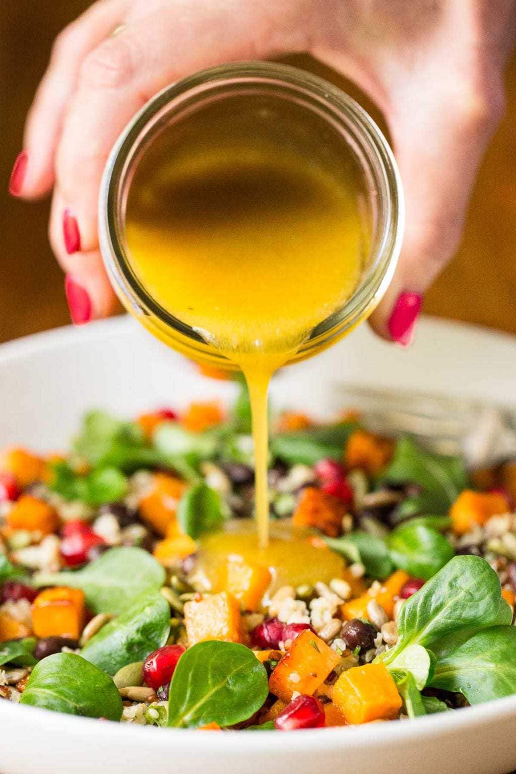 Close up vertical photo of Sweet Potato Quinoa Salad with dressing being poured from a jar over the salad.