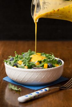 Vertical picture of a green salad in a white bowl with mango dressing poured on top