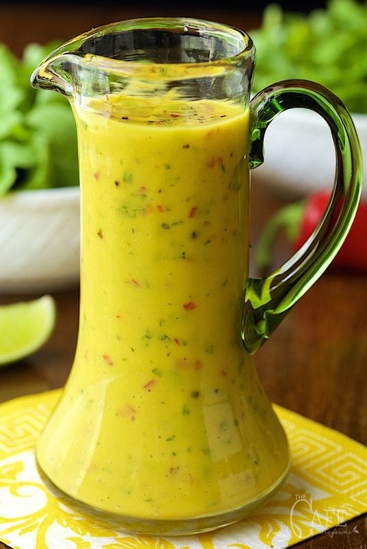 Photo of a contemporary glass pitcher filled with Sweet and Spicy Mango Salad Dressing on a yellow and white patterned napkin.