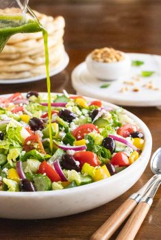 Vertical picture of the best greek salad in a white bowl with dressing poured on over top