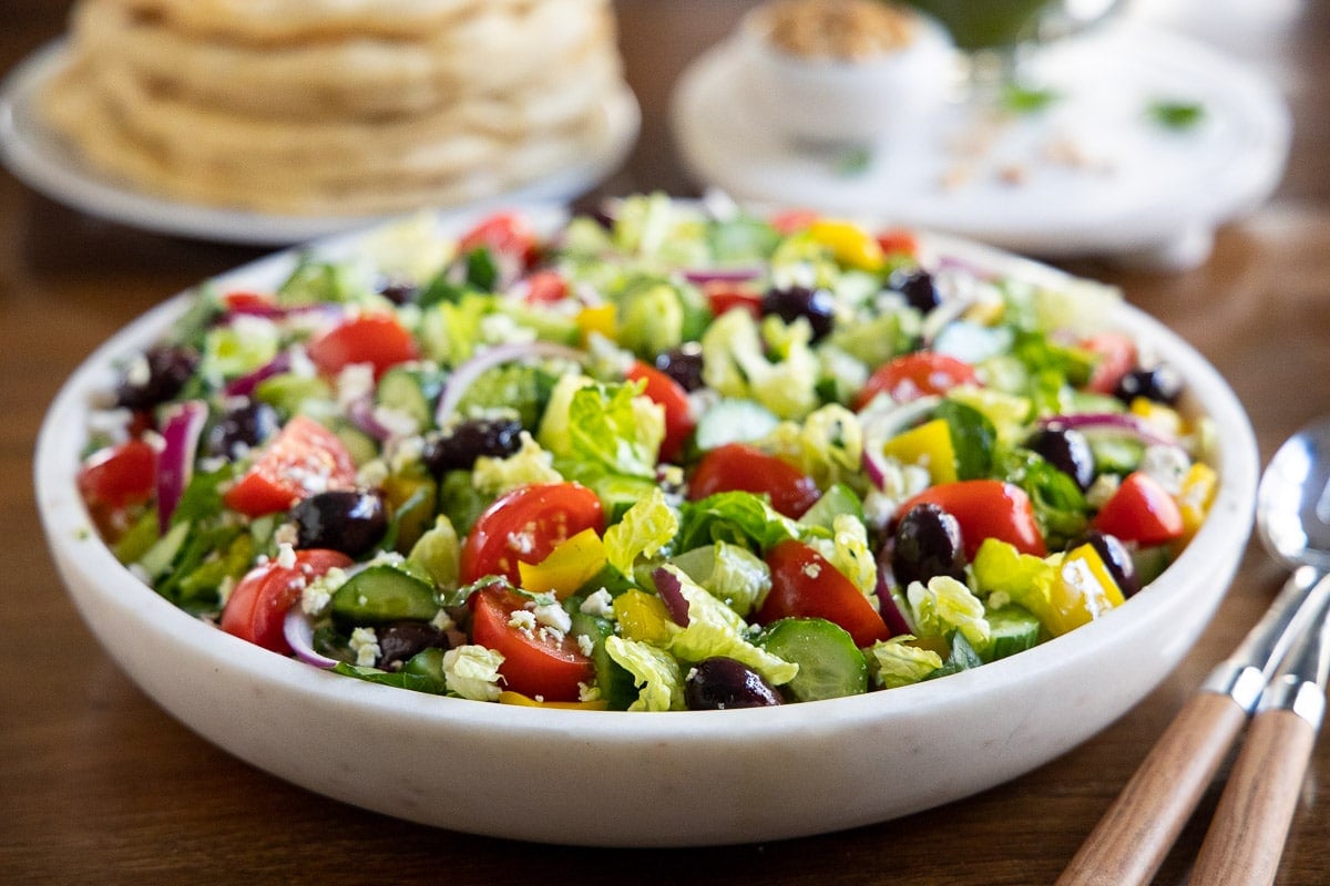 Horizontal closeup photo of a Best Greek Salad in a white marble serving bowl.