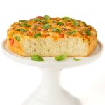 Vertical picture of Tomato, Basil, Parmesan Focaccia on a white stand on a white background