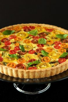 Vertical picture of Tomato, Basil and Fresh Mozzarella Tart on a glass stand on a black background
