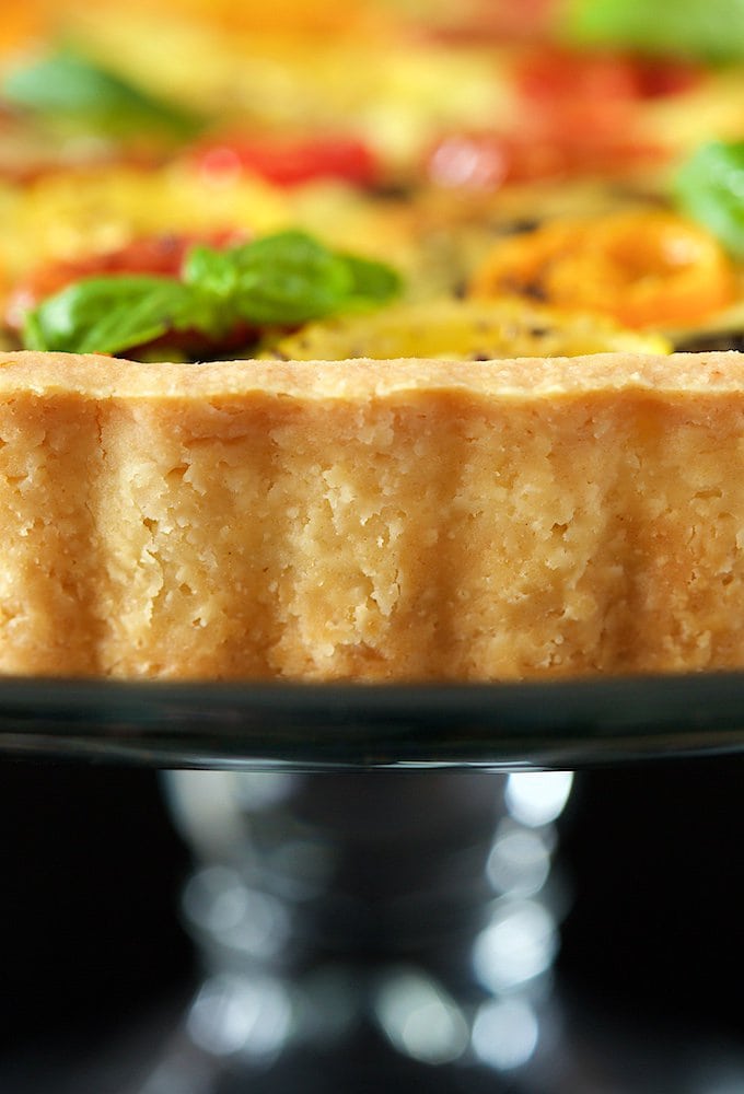 Closeup side shot of the crust of a Tomato Basil Fresh Mozzarella Tart on a glass cake stand.