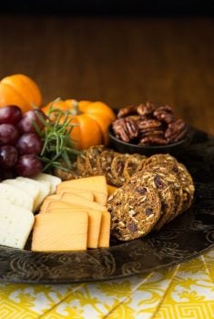 Vertical picture of Trader Joe's Pumpkin Cranberry Crisps in a platter with cheese, grapes, nuts and pumpkins