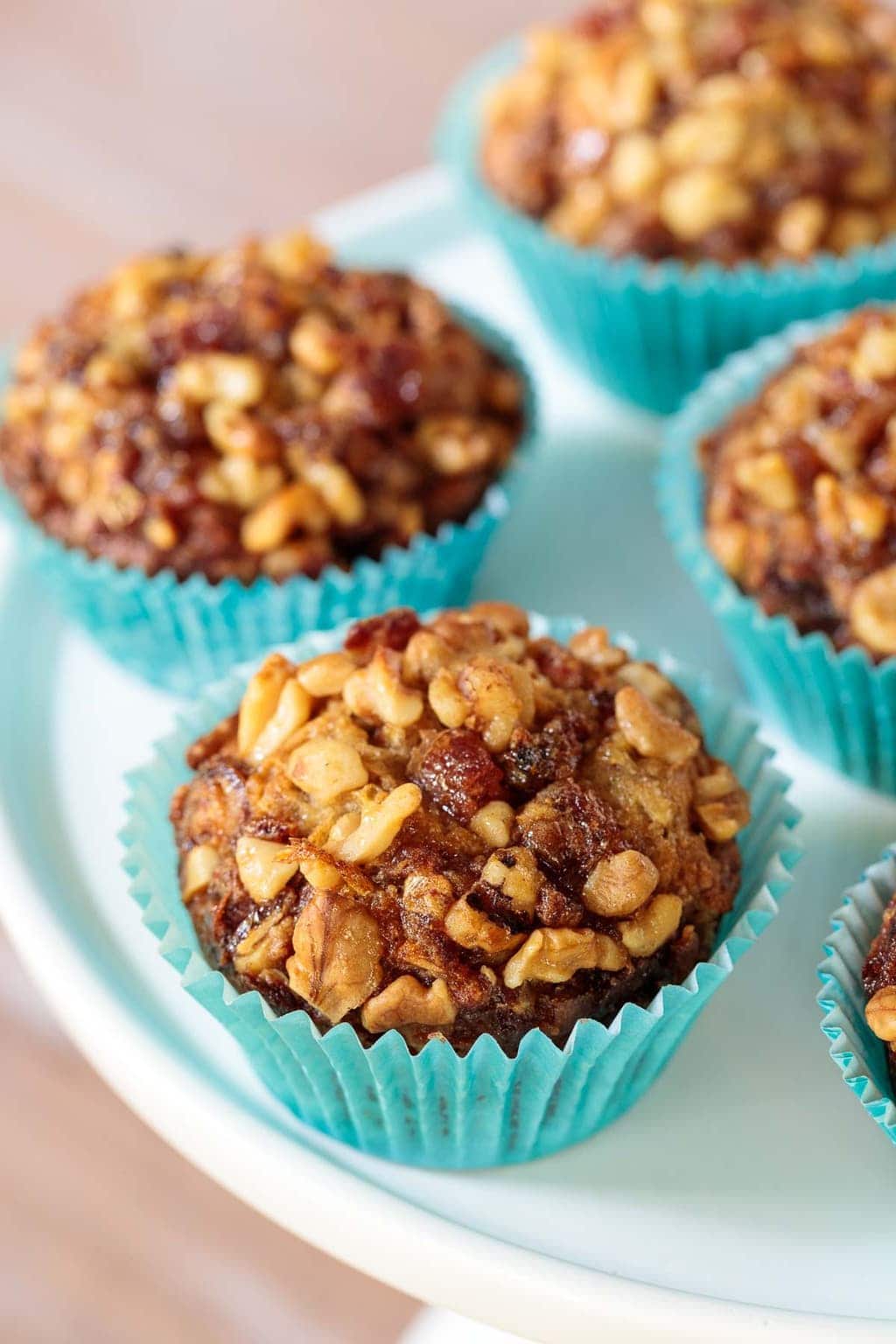 Vertical closeup photo of Walnut Date Banana Muffins in turquoise wrappers on a white cake stand