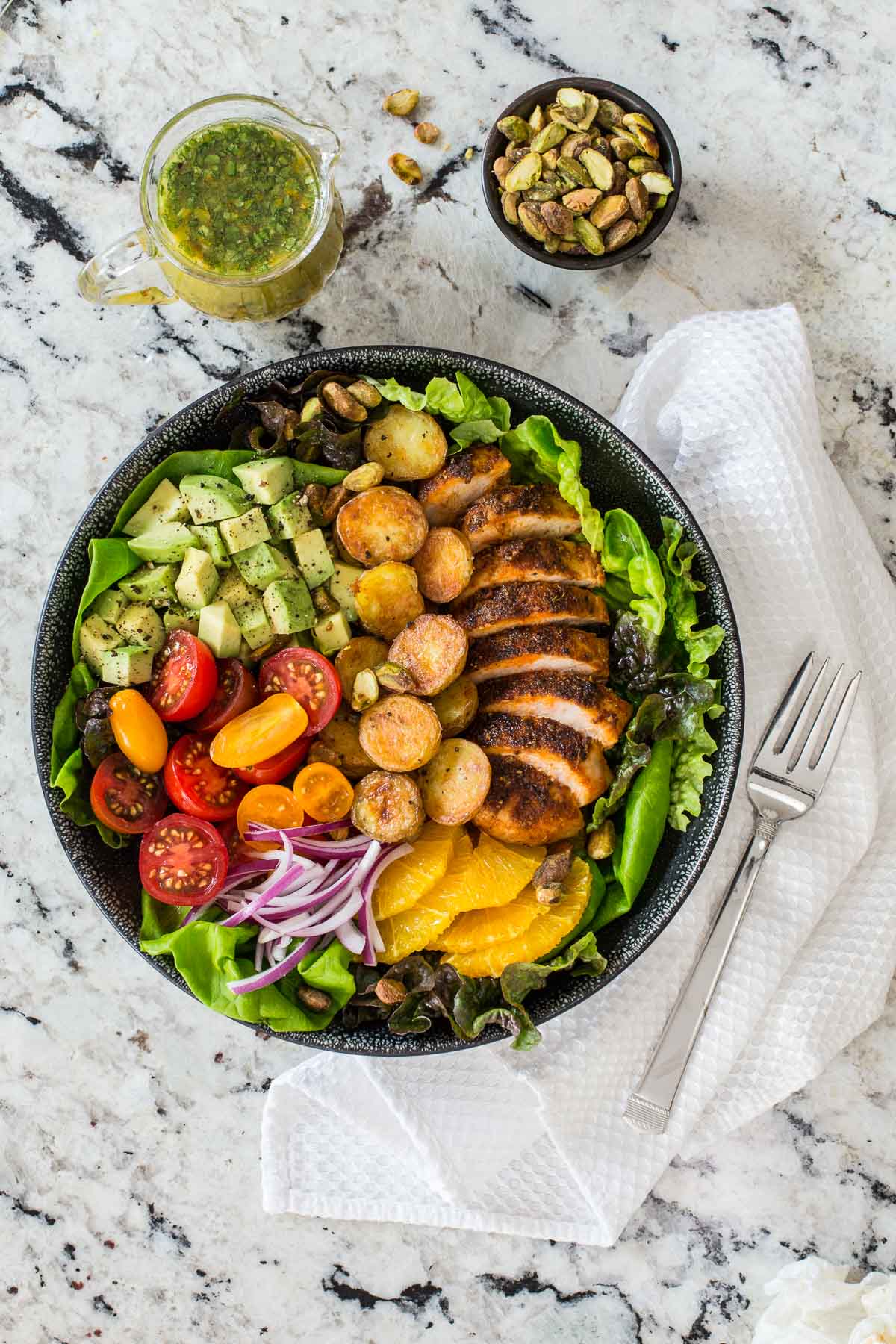 Vertical overhead photo of a serving bowl of Warm Chicken and Roasted Potato Salad on a granite kitchen countertop.
