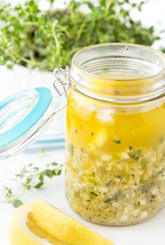 Vertical picture of Whole Lemon Salad Dressing in a glass jar with herbs
