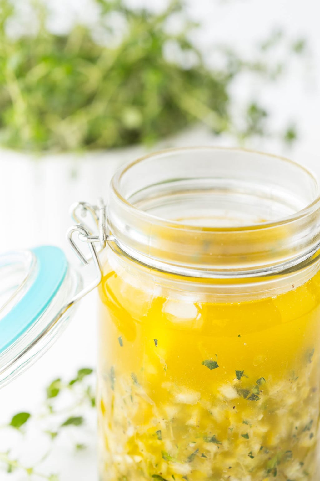 Photo of a glass jar of Whole Lemon Thyme Salad Dressing with a bowl of fresh thyme in the background.