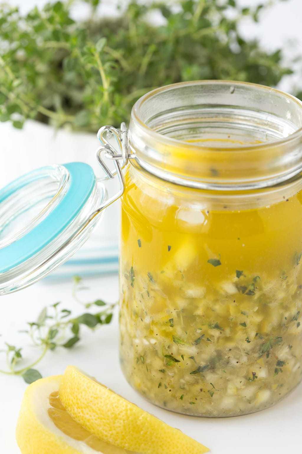 Vertical photo of Whole Lemon Thyme Salad Dressing in a glass Ball jar with sprigs of thyme in the background and lemon wedges in the foreground.