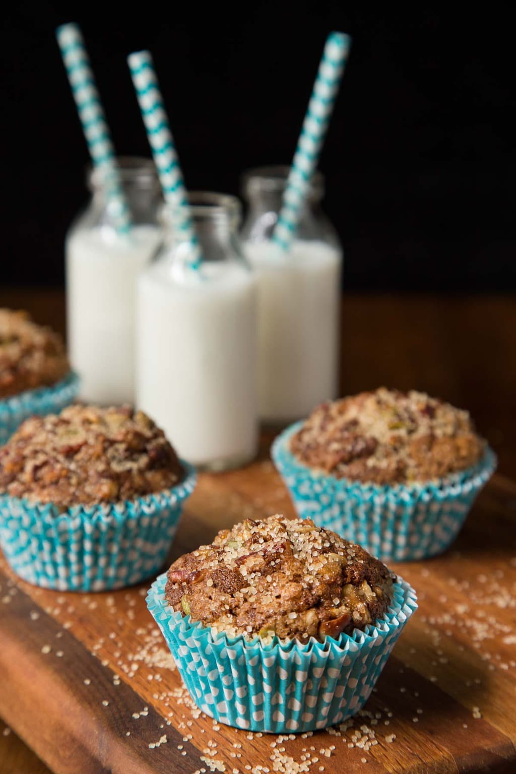 Vertical photo of Zucchini Morning Glory Muffins on a wooden cutting board with glass pints of milk in the background.