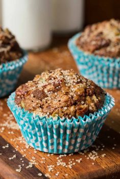 Vertical picture of Zucchini Morning Glory Muffins in turquoise muffin wrapper on a wooden cutting board