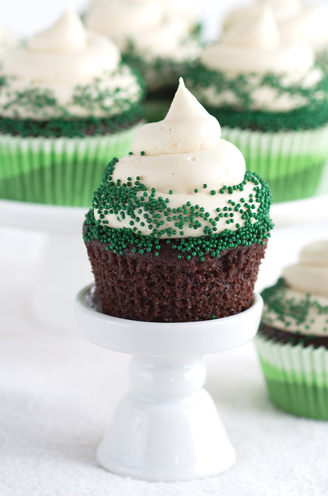 Photo of a Guinness Chocolate Cupcake on a white stand with a platter of cupcakes in the background.