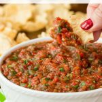 Vertical photo of a white bowl filled with Best Ever Super Easy Salsa with tortilla chips in the background.
