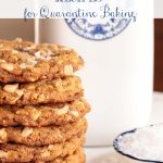 Vertical photo of a stack of Oatmeal Toffee Peanut Butter Cookies with a jar of milk and a dish of sea salt in the background.