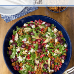 Overhead vertical photo of an Arugula Roasted Grape Salad in a navy blue serving bowl on a wood table.