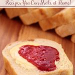 Vertical photo of a slice of Homemade Bread spread with butter and raspberry jam on a wooden cutting board with the rest of the slices in the background.