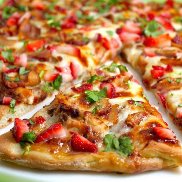 Closeup photo of a slice of Strawberry Balsamic Pizza with Chicken and Applewood Bacon with an entire pizza in the background.