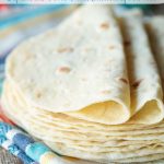 Vertical photo of a stack of Homemade Flour Tortillas on a multi-colored towel.