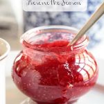 Vertical closeup photo of a jar of Strawberry Freezer Jam with jam spilling over the front of the jar.