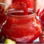 Vertica photo of a glass Weck jar of Strawberry Freezer Jam surrounded by fresh strawberries.