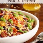 Vertical photo of a white bowl of Slow Roasted Tomato Ancient Grain Salad on a wood table.