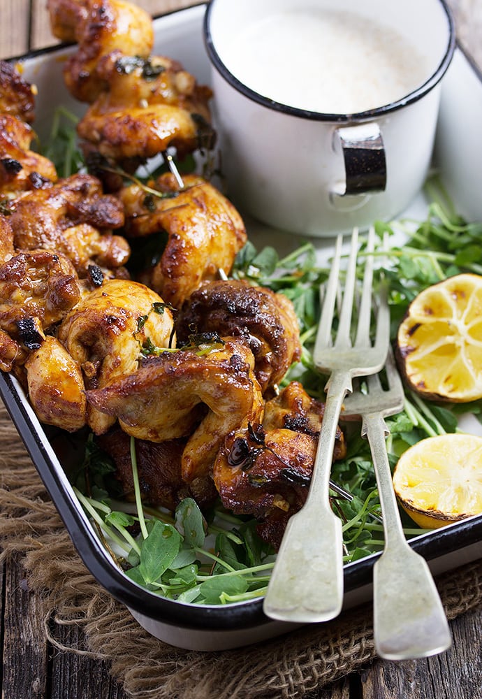 Vertical image of Portuguese Chicken Skewers in a white pan with greens and two forks.