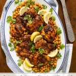 Vertical overhead photo of Charred Honey Lemon Chicken with Crispy Chickpeas on a white oval platter with graphics, "Winner, Winner Chicken Dinner!" at the bottom of the photo.