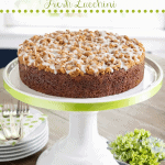 Vertical photo of an Easy Zucchini Crumb Cake on a white pedestal cake stand with green ribbon trim.